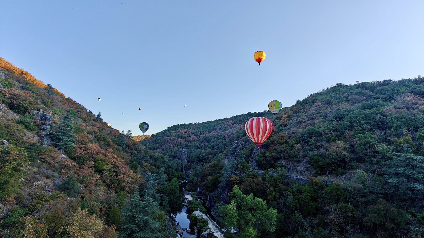 Plusieurs montgolfières colorées volant au-dessus d’une vallée verdoyante en Ardèche